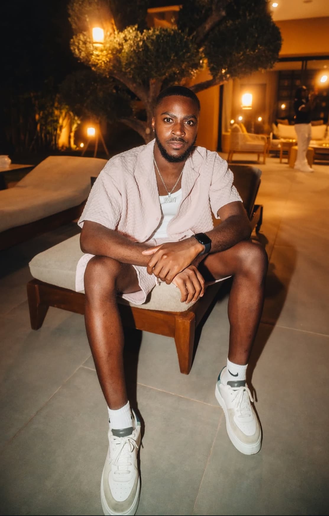Man in a pink textured outfit sits on a lounge chair outdoors at night.