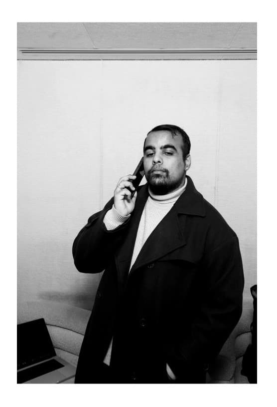 Bearded man in a dark overcoat and turtleneck sweater talking on a mobile phone.